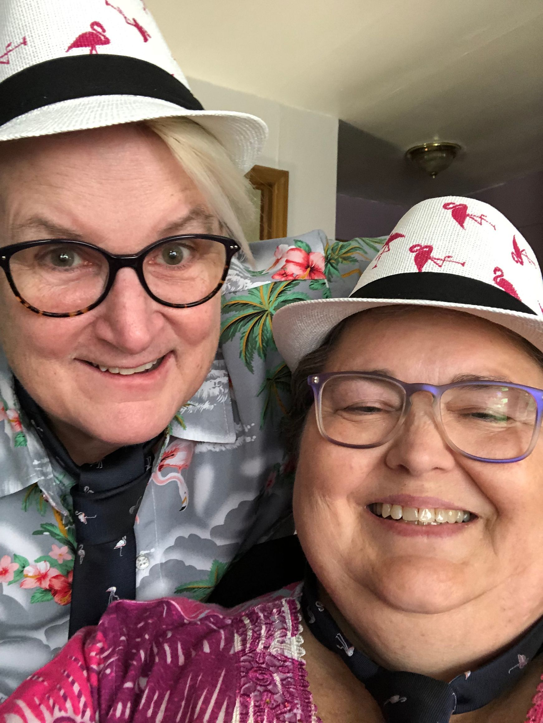 Two people wearing matching flamingo-print fedoras and ties, smiling closely at the camera.