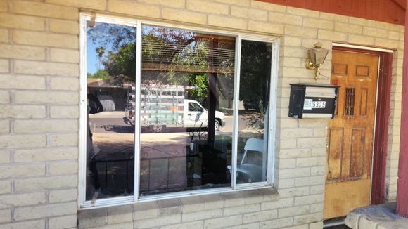 Balcony with a large window overlooking a city. Red brick walls, white trim, and a blue sky.