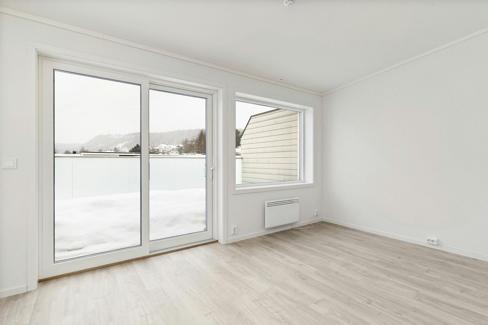 Empty room with large windows overlooking snowy landscape and light wood floors.