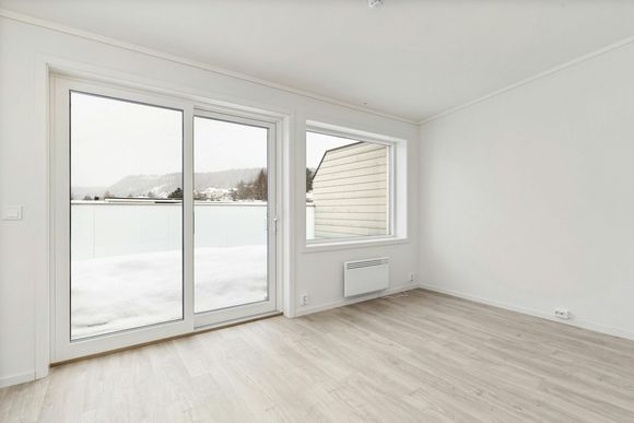 Empty room with large windows overlooking snowy landscape and light wood floors.
