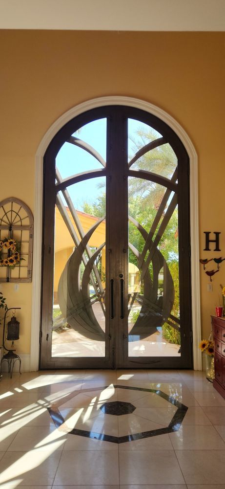 Arched front door with decorative metalwork and surrounding peach-colored walls. Sunlight streams through the glass.
