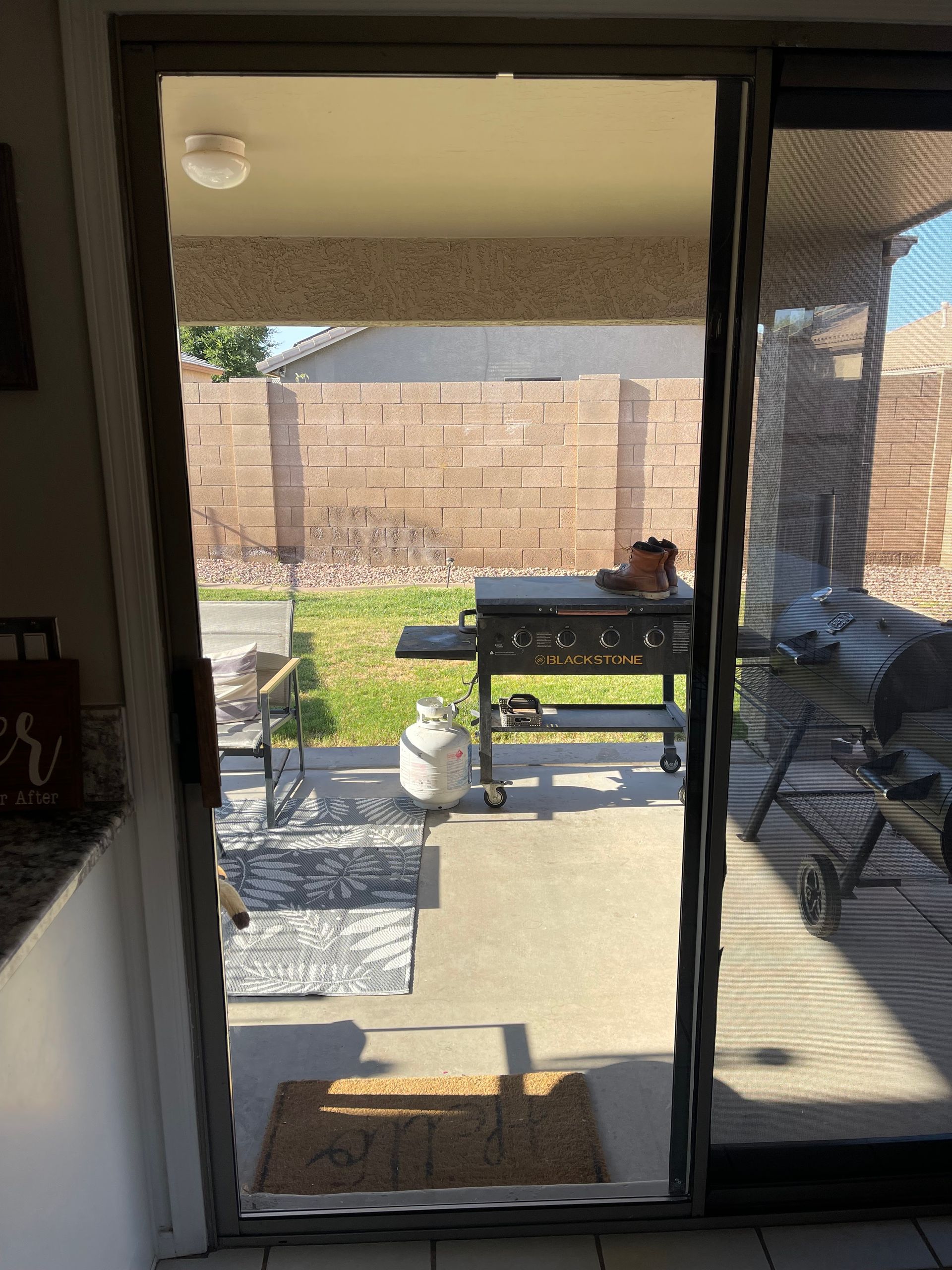 Sliding glass door open to a backyard patio with a grill and brick wall.