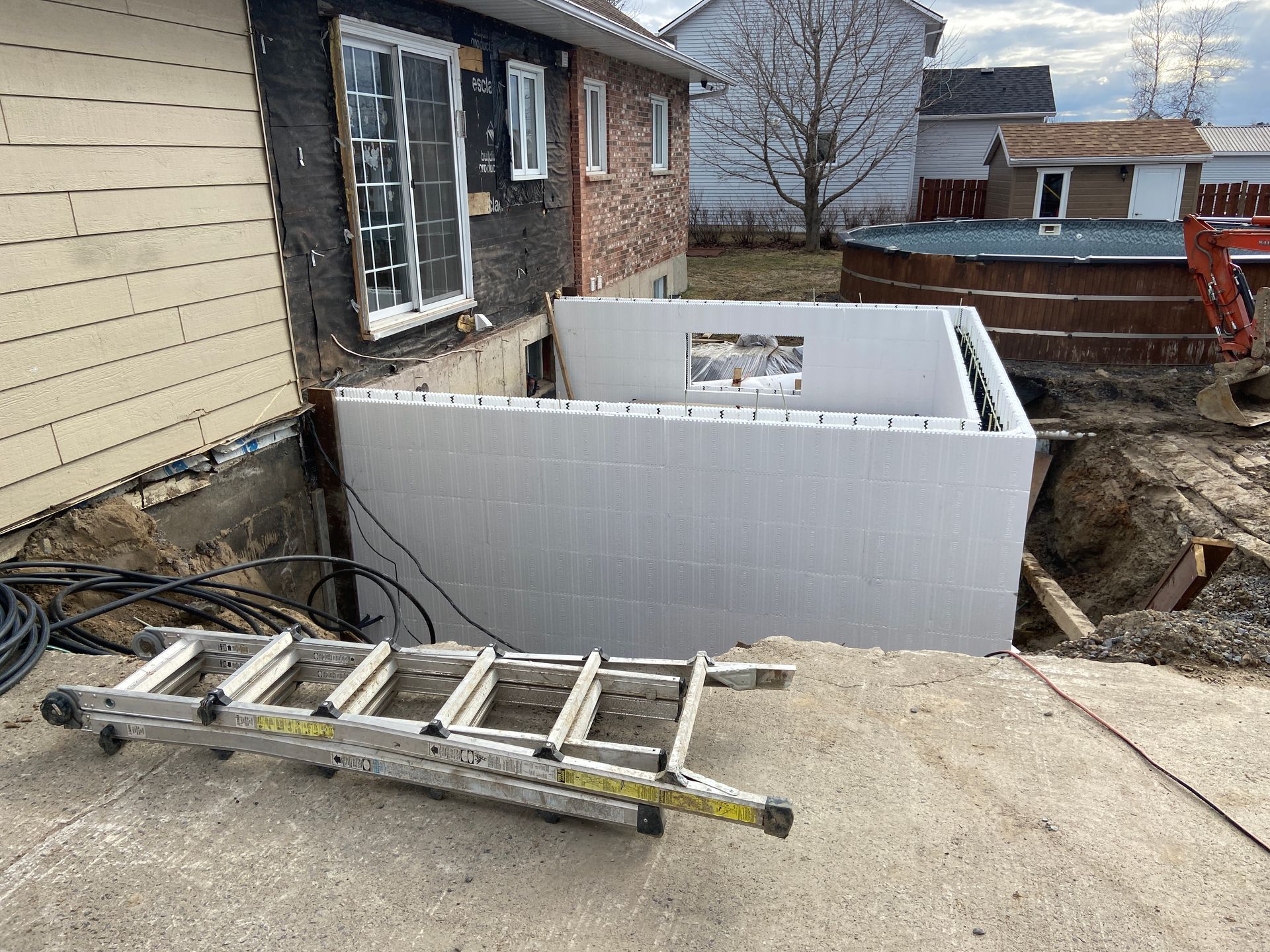 Une échelle est posée sur le trottoir devant une maison en construction.