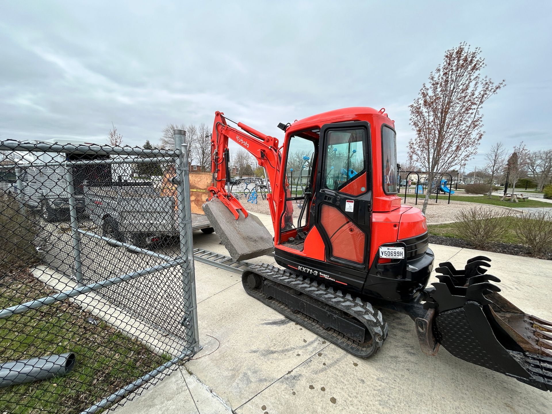 Une petite excavatrice rouge est garée à côté d'une clôture grillagée.