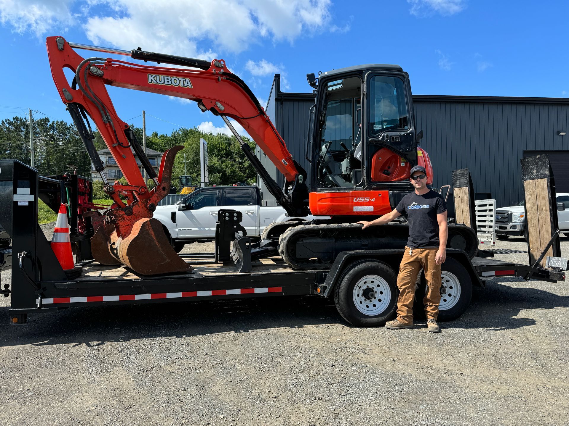 Un homme se tient à côté d'une excavatrice sur une remorque.