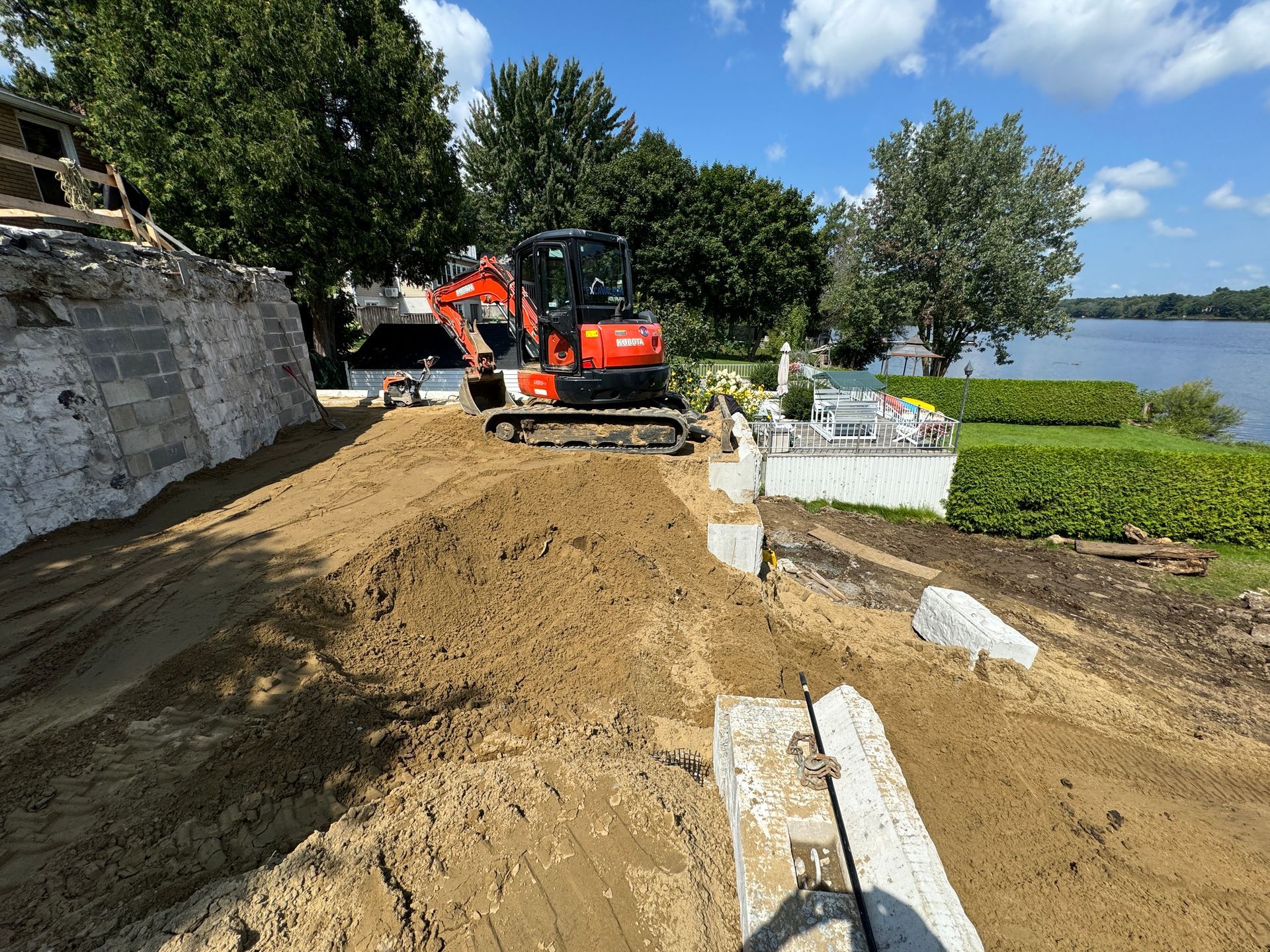 Une excavatrice rouge roule sur un chemin de terre à côté d'un plan d'eau.