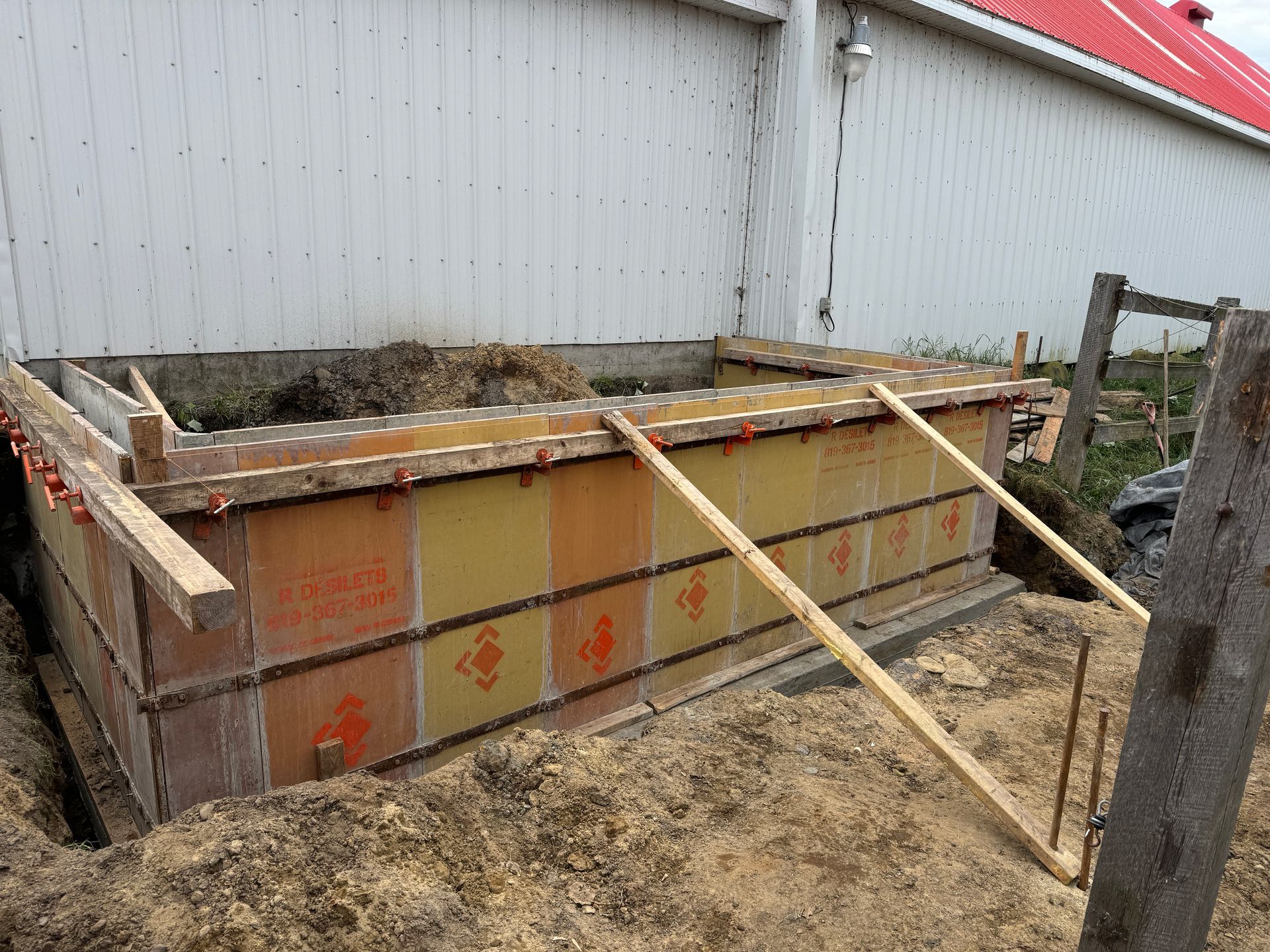 Un mur de béton est en train d'être construit devant un bâtiment blanc avec un toit rouge.