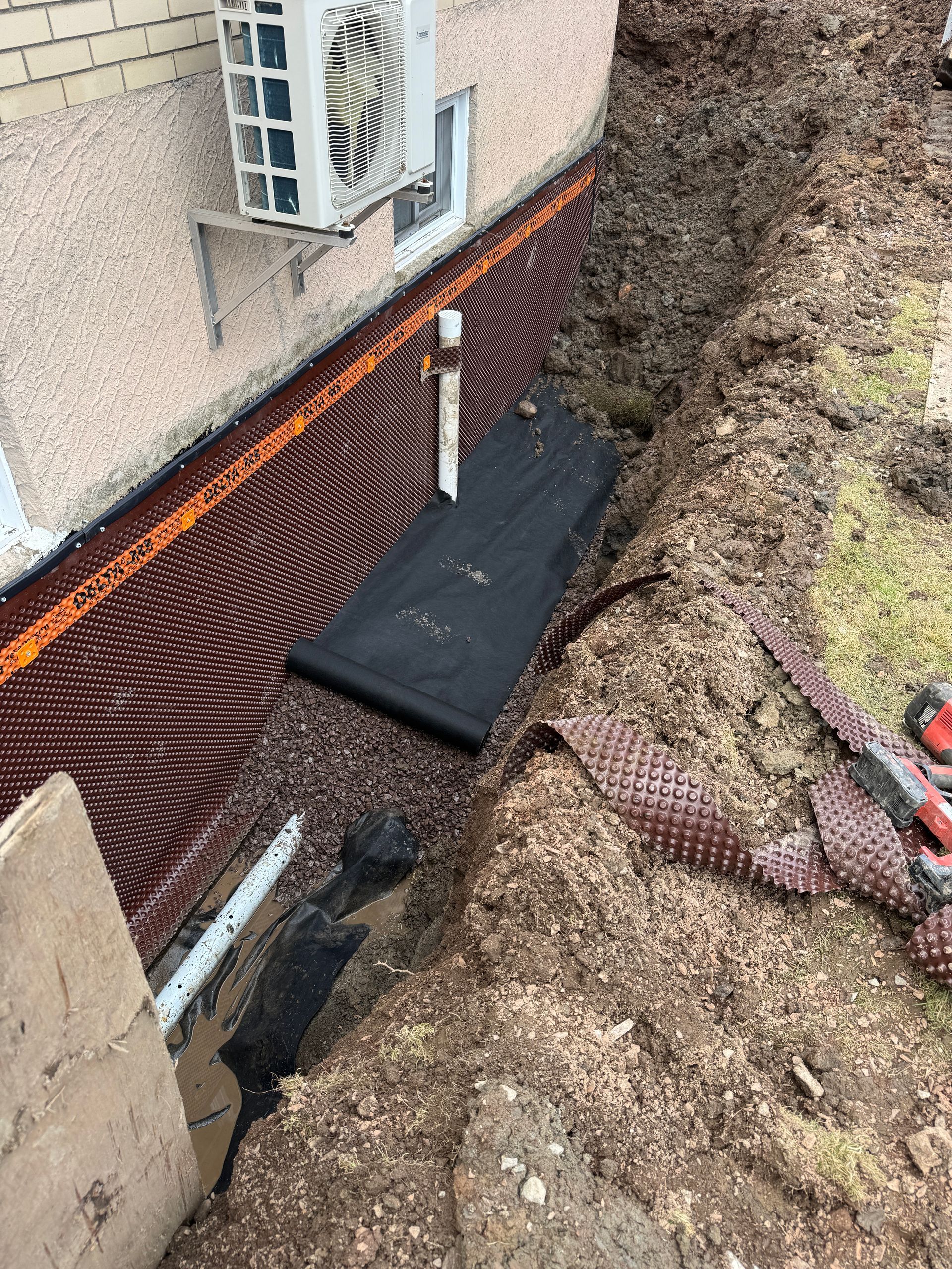 Un système de drainage est en cours d'installation sur le côté d'un bâtiment.
