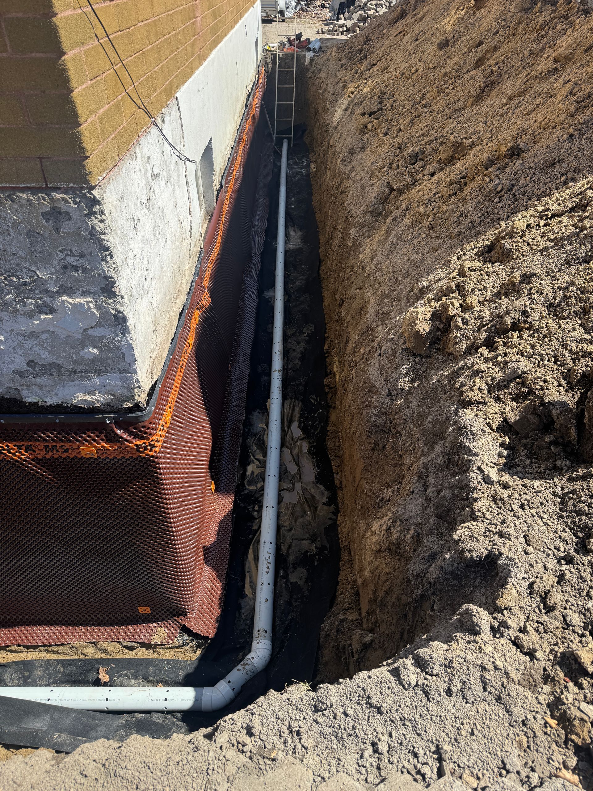 Un tuyau est en train d'être installé dans une tranchée à côté d'une maison.