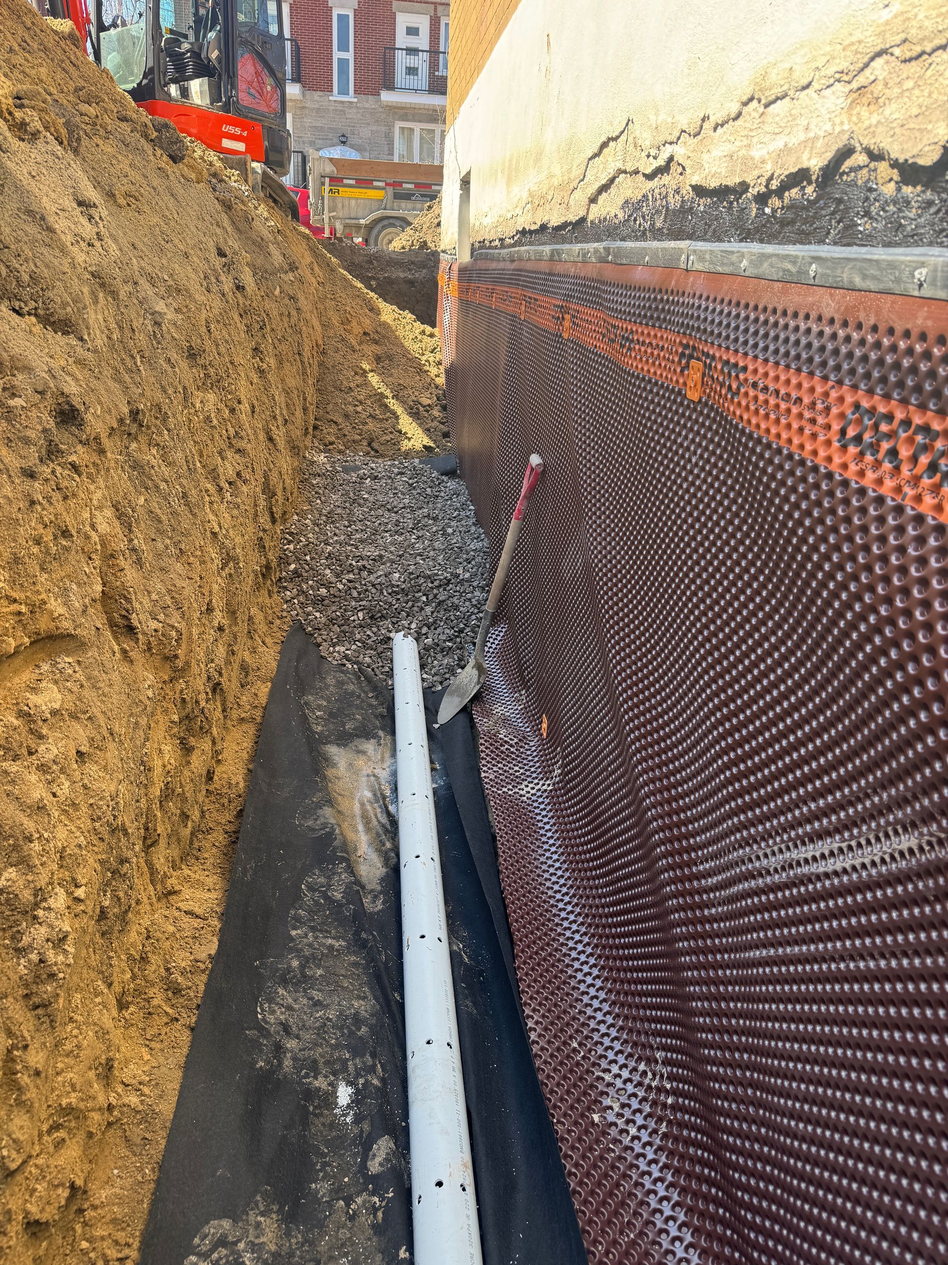 Une excavatrice rouge est assise sur le trottoir à côté d'une clôture grillagée.