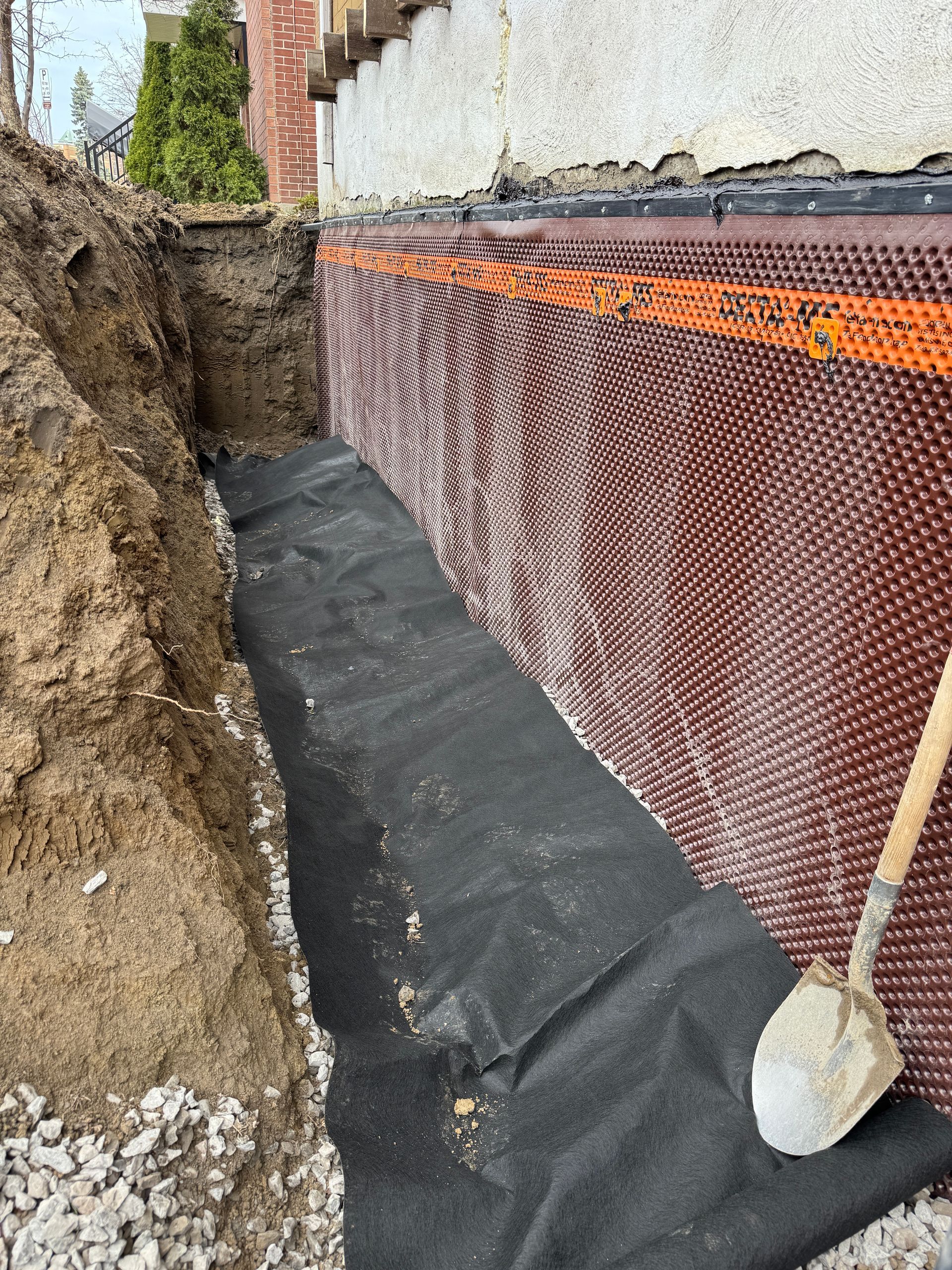 Une pelle est posée sur un tas de terre à côté d'un mur.