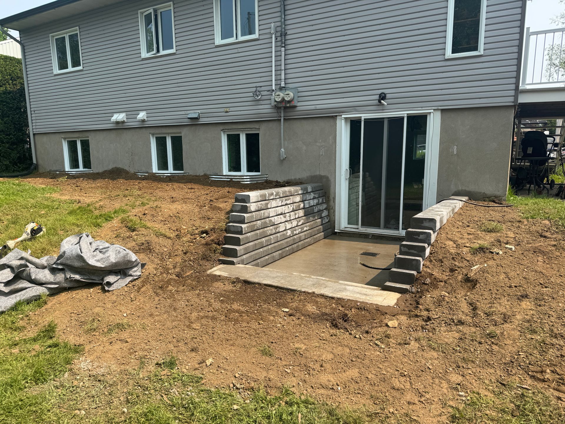 Une maison avec une porte coulissante en verre est située au sommet d'une colline de terre.