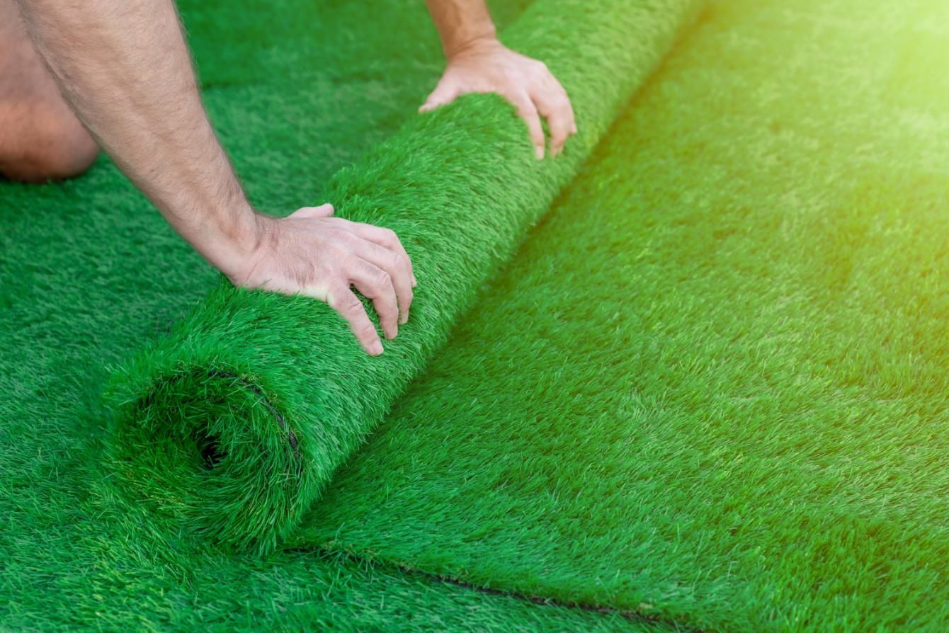 Person rolling out a large roll of artificial green turf.