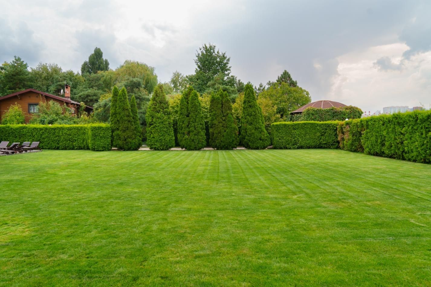 Green lawn bordered by hedges and trees, cloudy sky overhead.