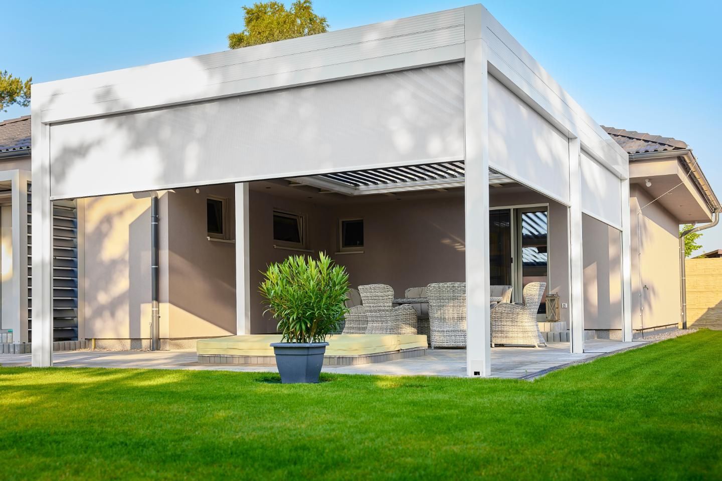 White pergola with retractable shade, attached to a house with green lawn.