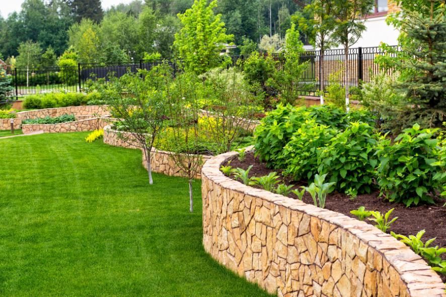 Lush green lawn and tiered garden beds with stone walls, filled with plants and trees.