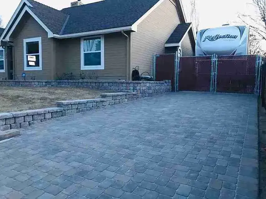 Driveway of a home paved with interlocking bricks, leading to a fenced RV storage area.