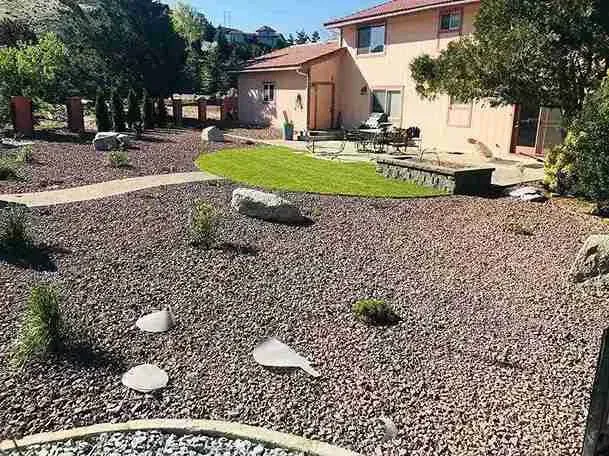 Backyard with gravel ground cover, a patch of green grass.