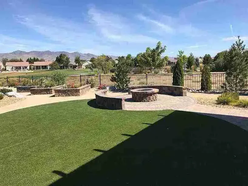 Backyard with a fire pit, artificial turf lawn, landscaping, and a view of mountains under a blue sky.