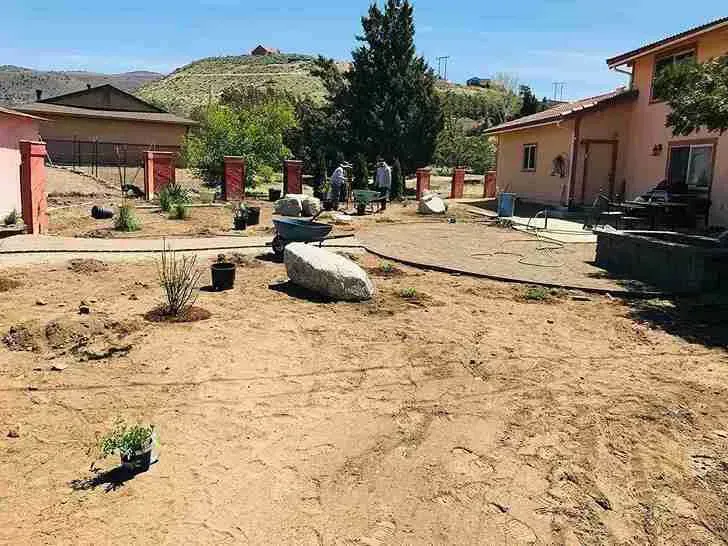 A front yard with landscaping under construction, boulders, plants, and a light pink house.