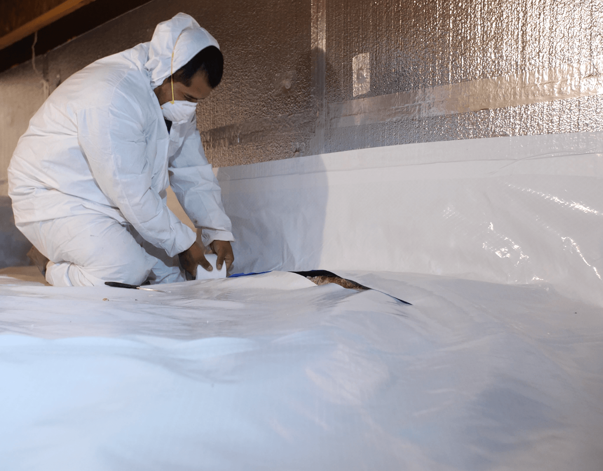 A man in a white suit is kneeling on a white sheet of plastic.