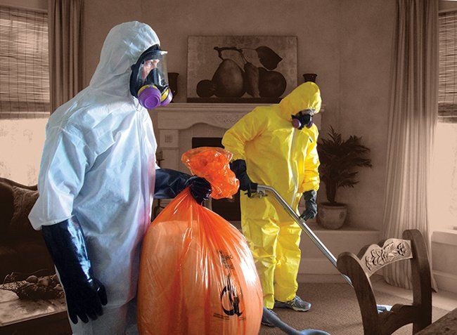 Two men in protective suits are cleaning a living room.
