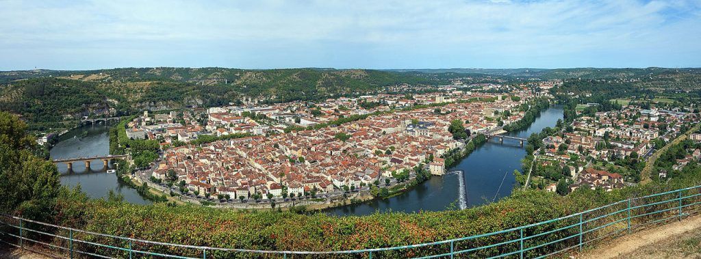 Panoramic aerial view of a city with a river curving through dense buildings and green trees