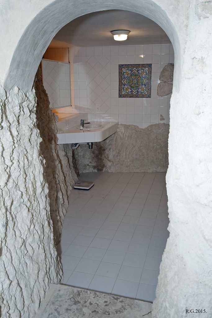 Small arched doorway leading into a narrow, white stone room with a sink and tiled floor.