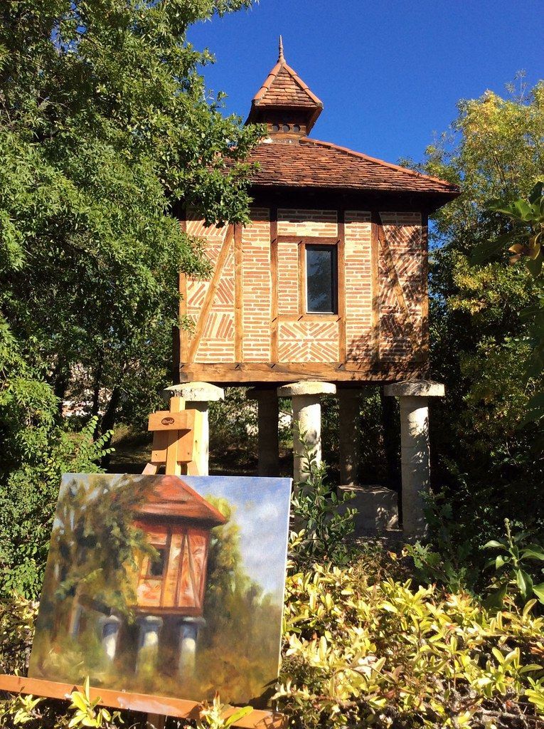Small wooden hut on stilts in a sunny garden, with a painted sign in front.