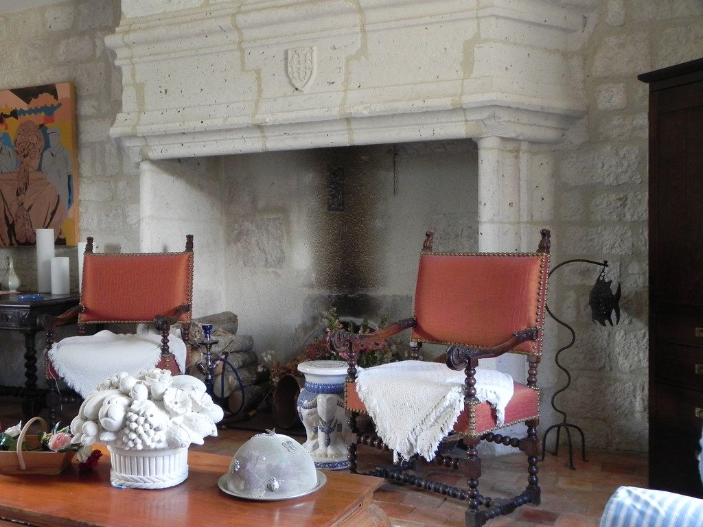 Living room with a large white fireplace, two red armchairs, and a coffee table with flowers and decor