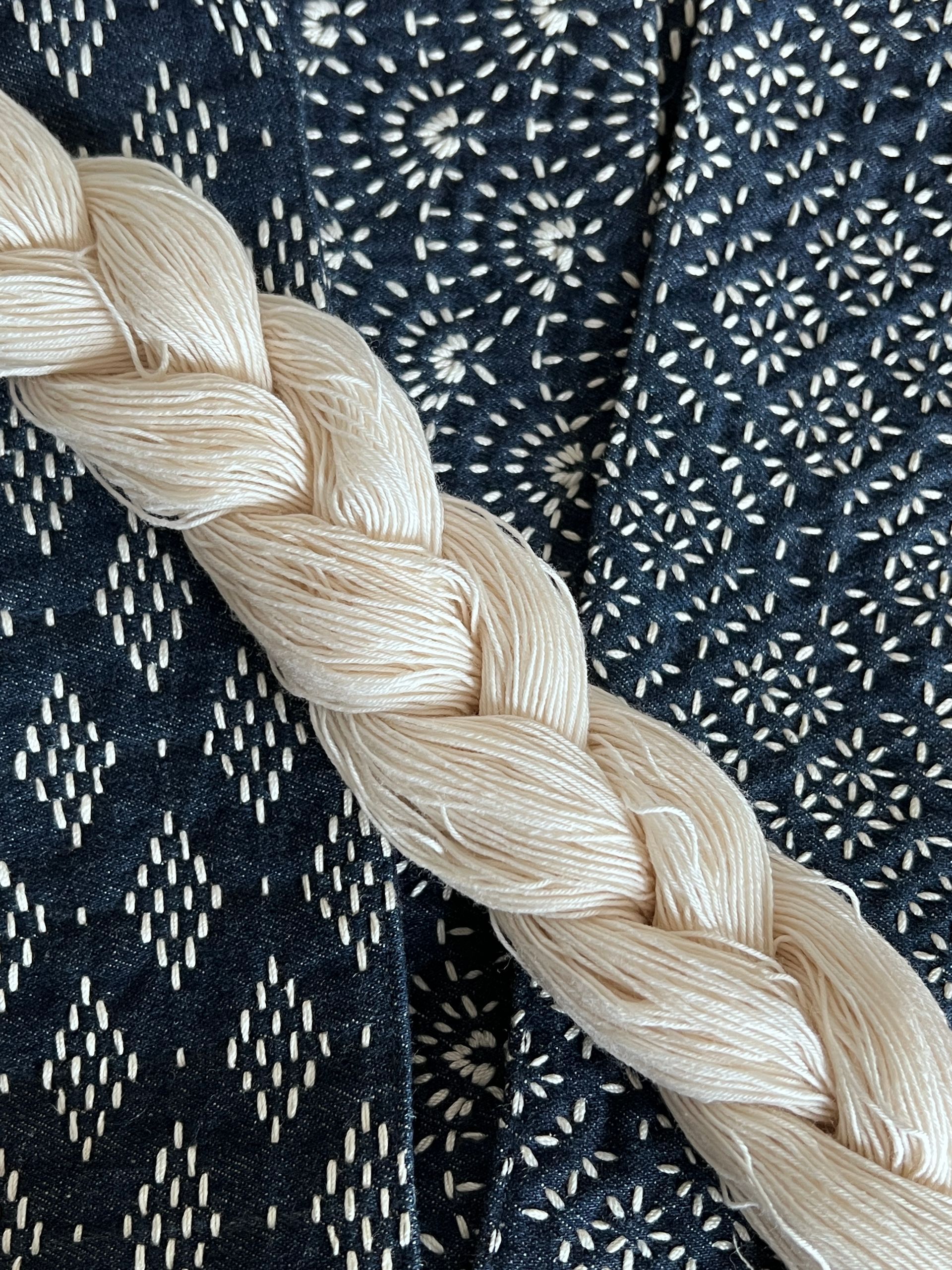 Close-up of a cream braided rope on dark blue patterned fabric.
