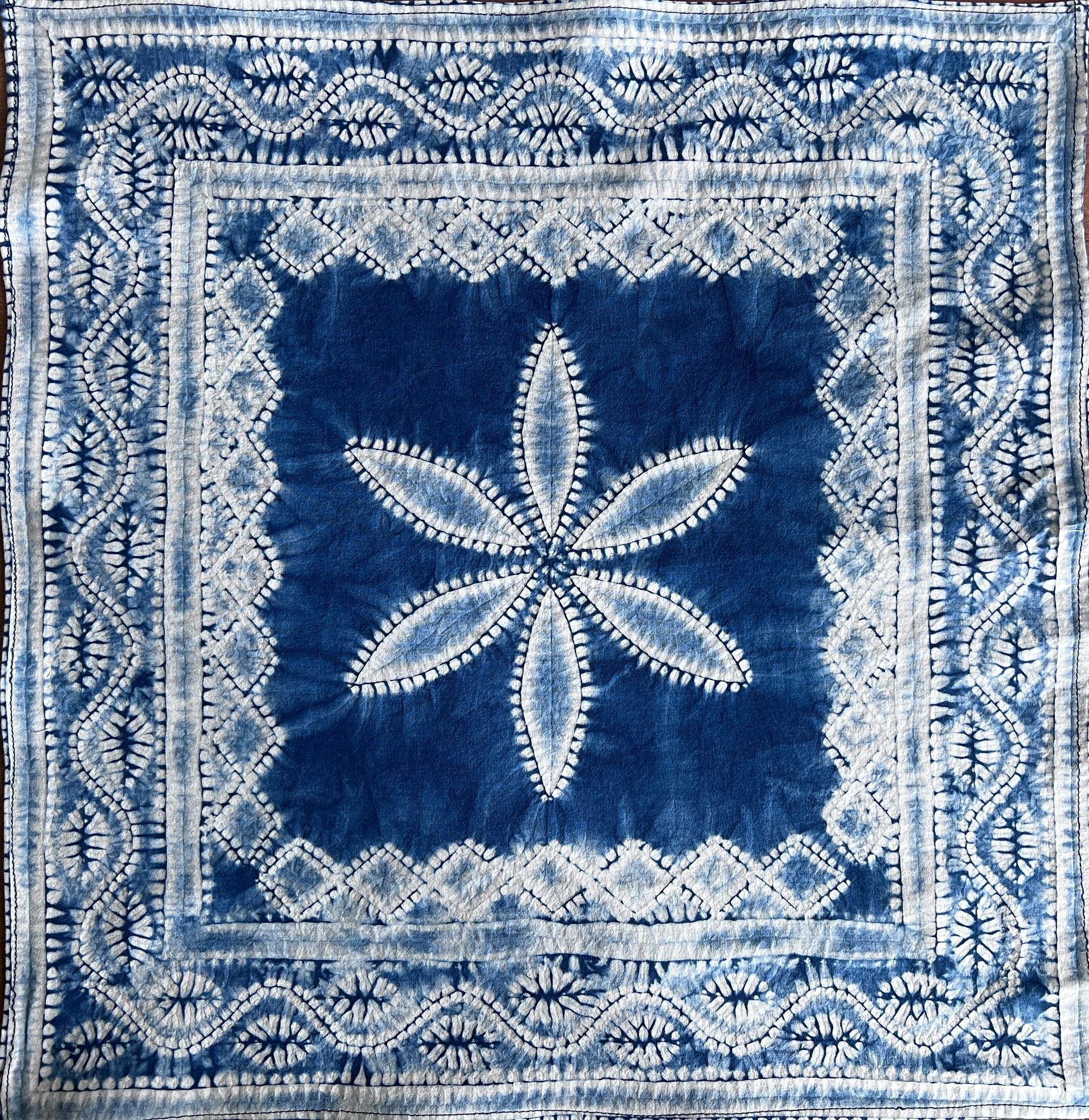Blue quilt square with a white embroidered flower and patterned border