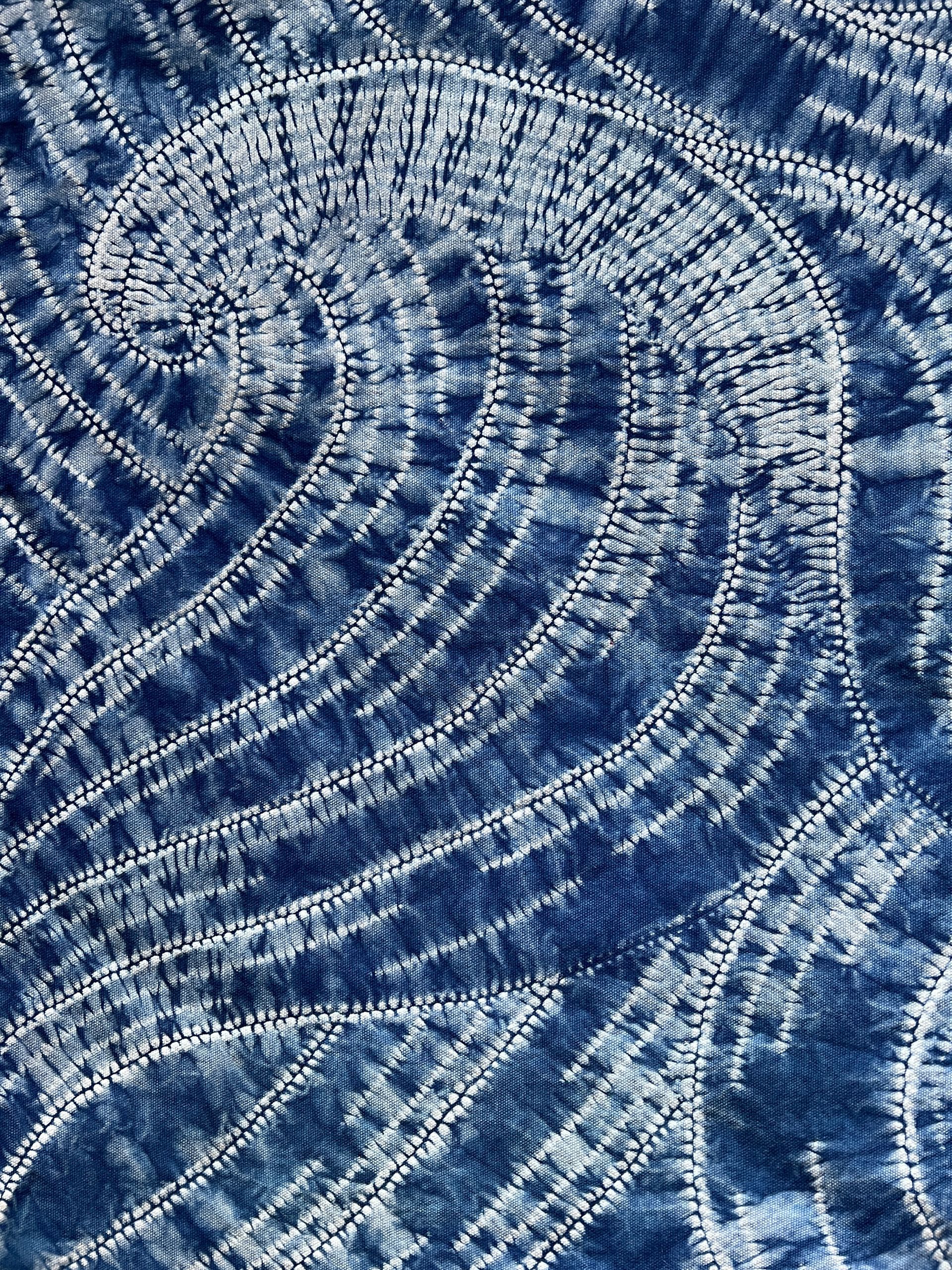 Close-up of blue textured fabric with swirling white stitched patterns