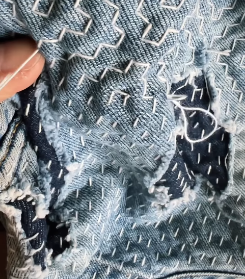 Close-up of a sashiko stitching with gray jean fabric with white stitching to mend jeans by  Silent Wave Studio
