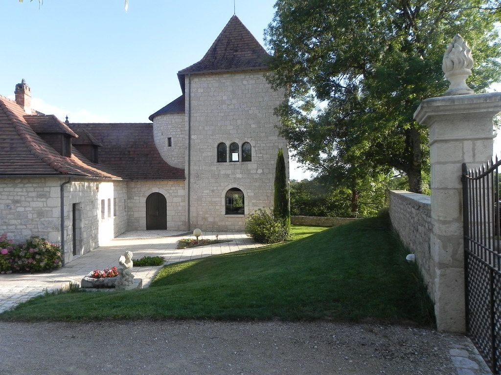 Stone castle tower and courtyard beside a sloped grassy hill, with trees and a wrought-iron gate.