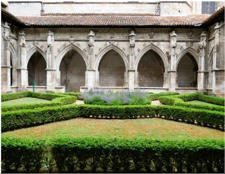 Stone cloister courtyard with Gothic arches and trimmed green hedges around a central lawn