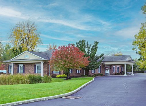 A large brick house with a driveway leading to it is surrounded by trees and grass.