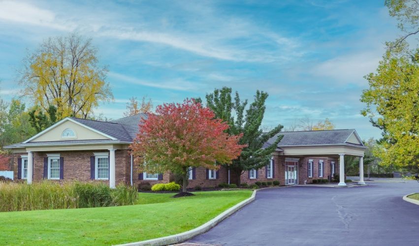 A large brick house with a driveway leading to it is surrounded by trees and grass.