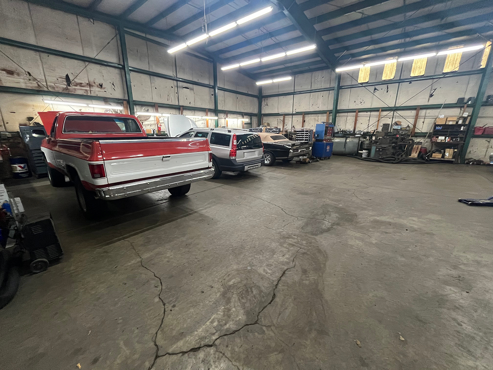 A red and white pickup truck parked in a large, industrial auto repair shop with concrete floors and overhead lighting.