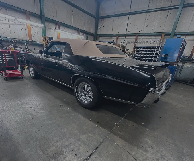 A black convertible muscle car with a tan soft top parked inside a metal-walled garage. | Maynard's Auto Repair Service