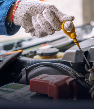 A gloved hand holding the yellow handle of a car engine oil dipstick to check the oil level. | Maynard's Auto Repair Service