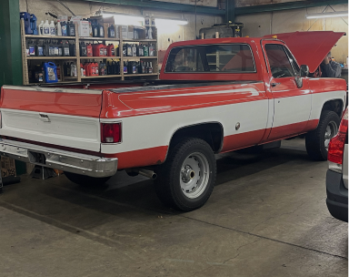 A red and white vintage Chevrolet pickup truck with its hood open in an auto repair garage. | Maynard's Auto Repair Service