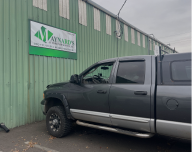 A gray pickup truck parked alongside a green metal-sided building with a Maynard's sign. | Maynard's Auto Repair Service