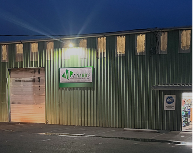 Green warehouse exterior at dusk with a Maynard's Construction sign. | Maynard's Auto Repair Service