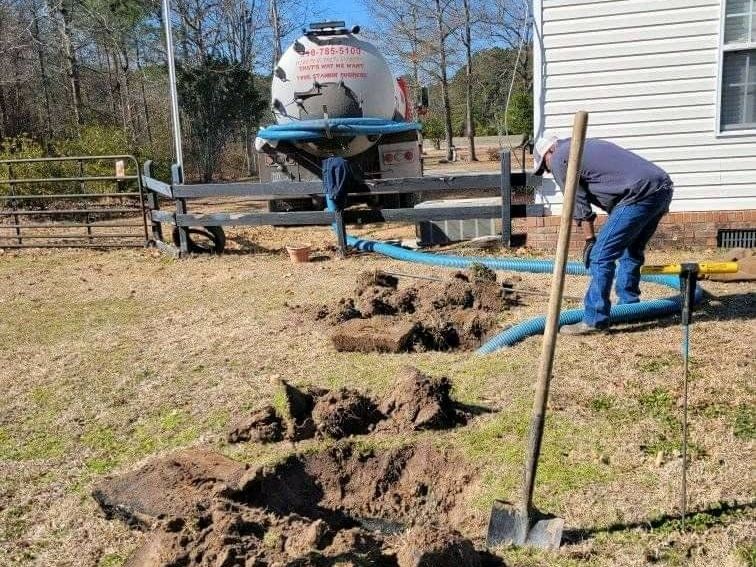 A man is digging a hole in the dirt in front of a house.