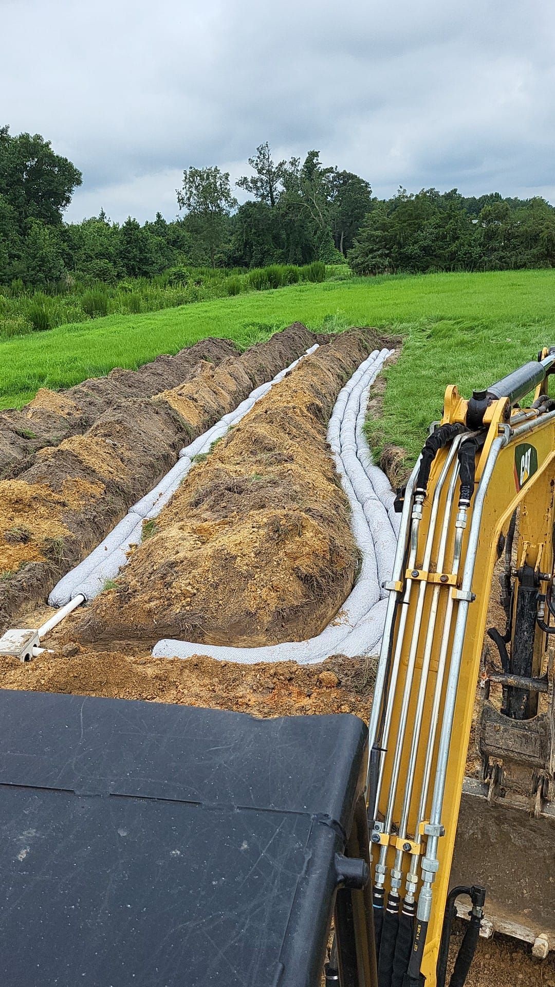 A yellow excavator is digging a trench in a field.