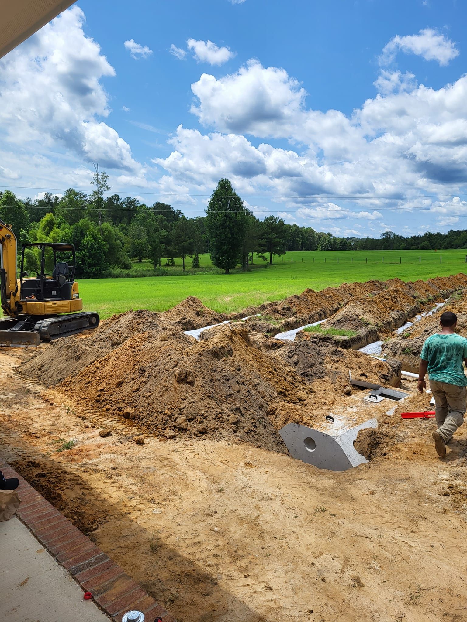 A man is walking through a dirt field with a bulldozer in the background.