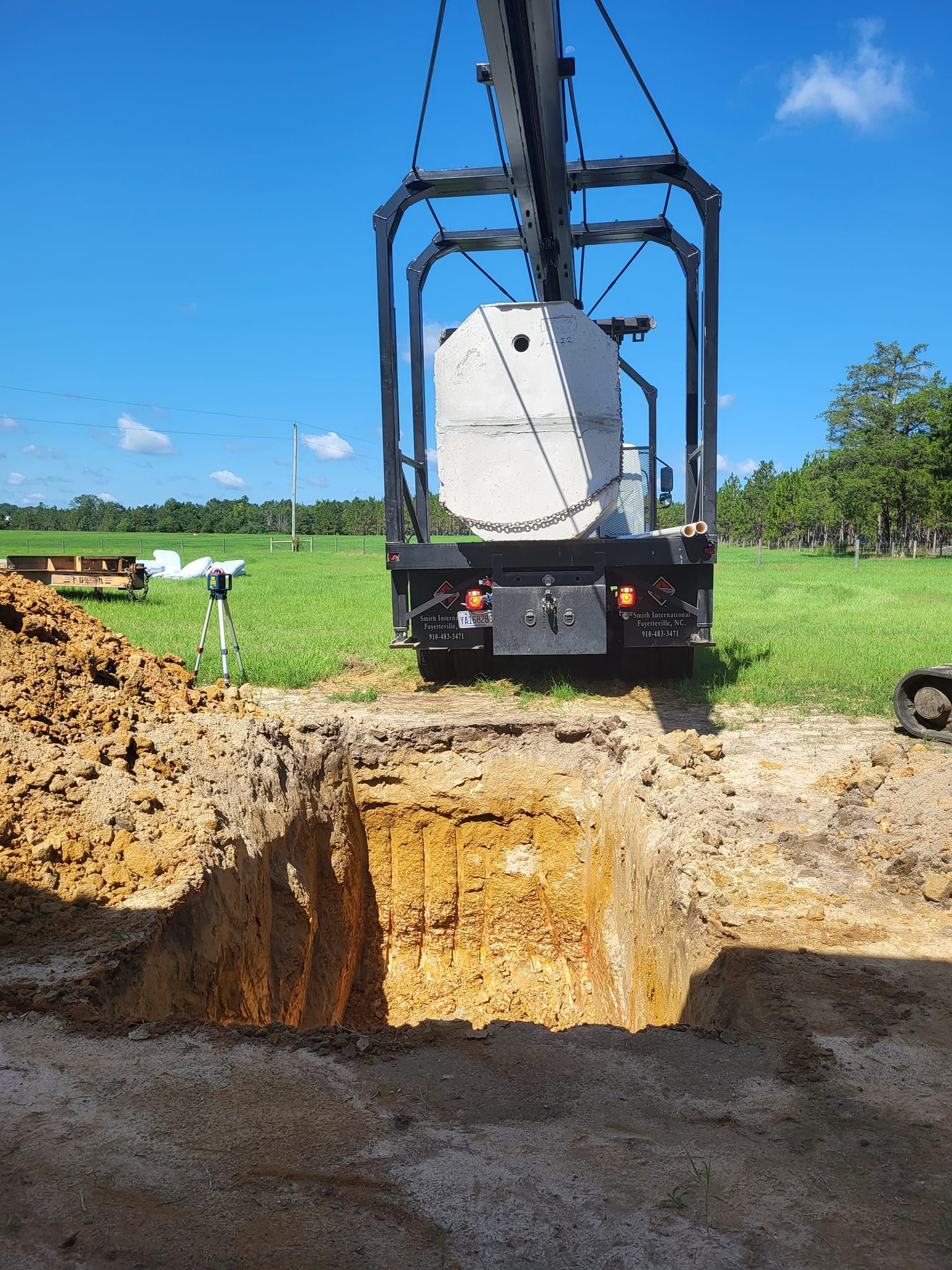 A crane is lifting a concrete block into a hole in the ground.