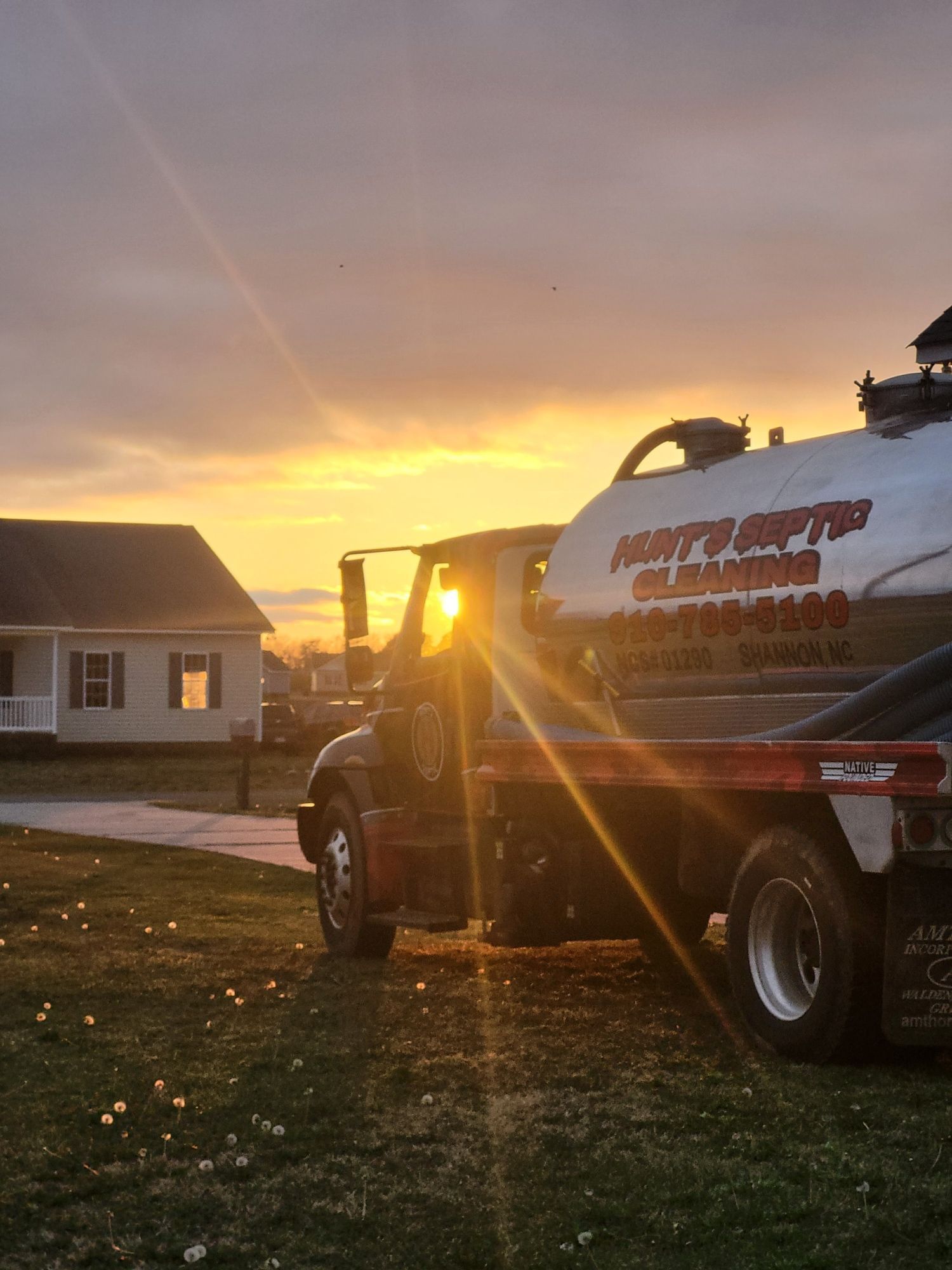 A vacuum truck is parked in front of a house at sunset