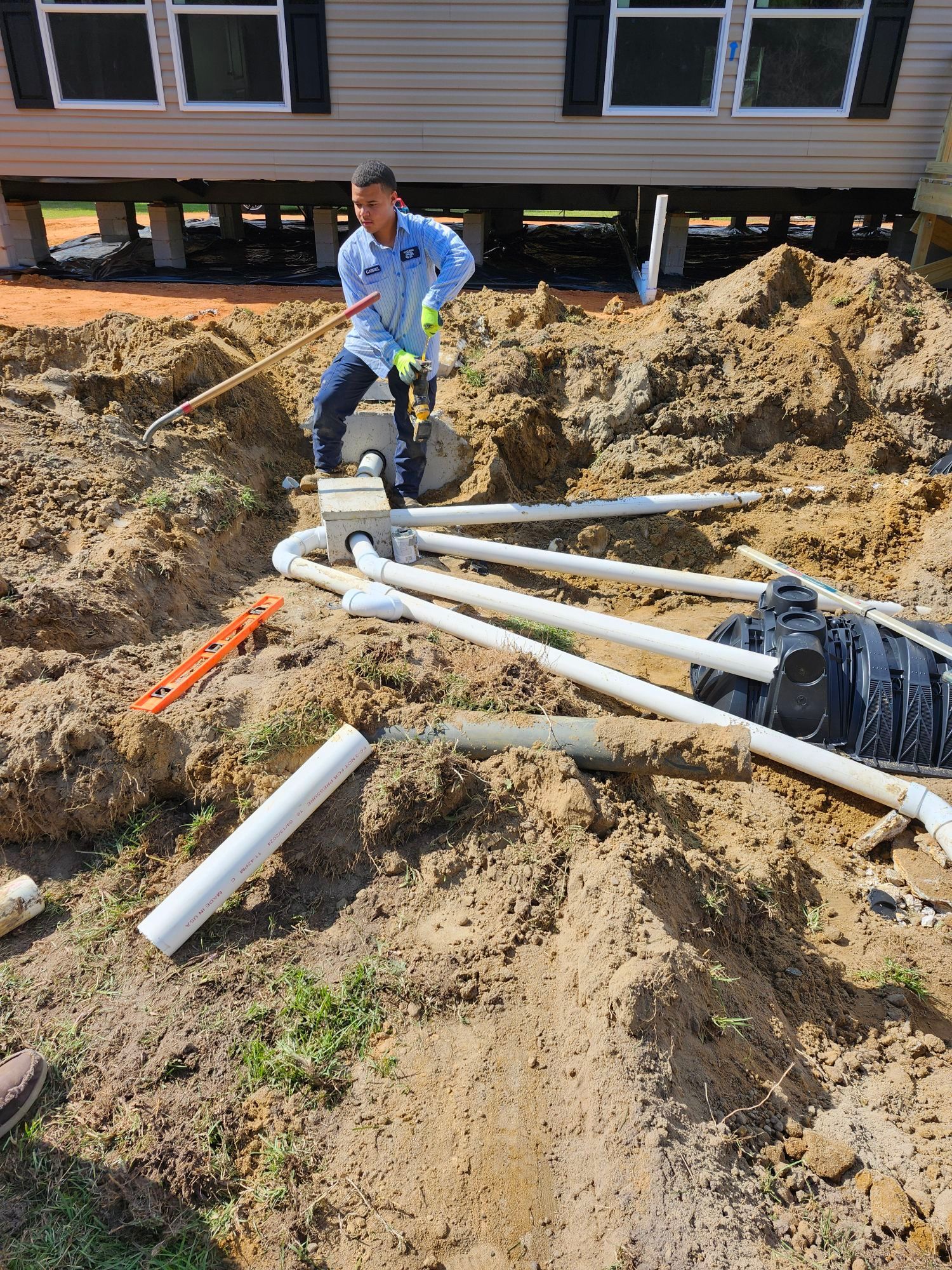 A man is working on a septic system in the dirt in front of a house.